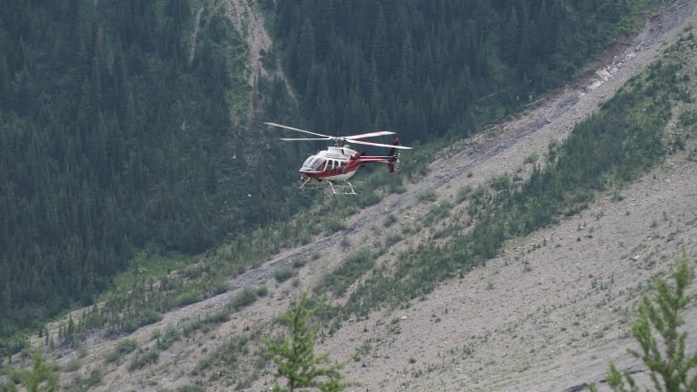 a red and white helicopter hovers over a mountain slope 