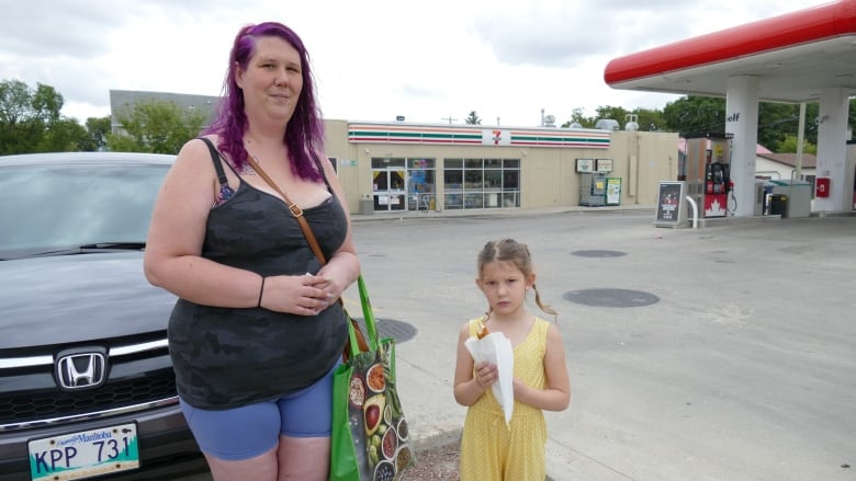 A woman with purple hair is standing next to a young girl. They are standing in front of a 7-Eleven store.