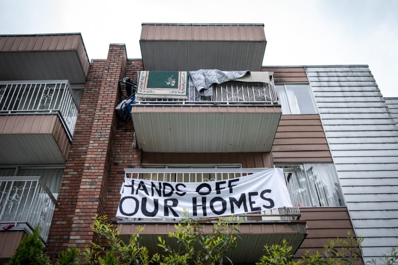 A sign reads 'Hands off our homes' on a balcony on an apartment building.