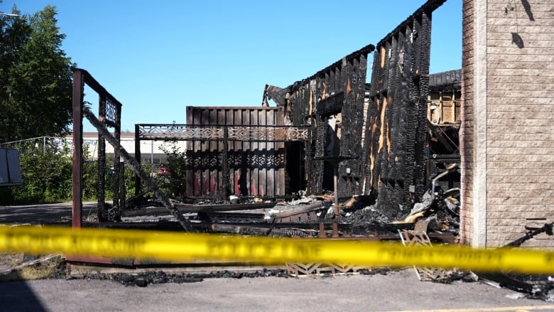 Police tape is in front of the remains of a burned building. 