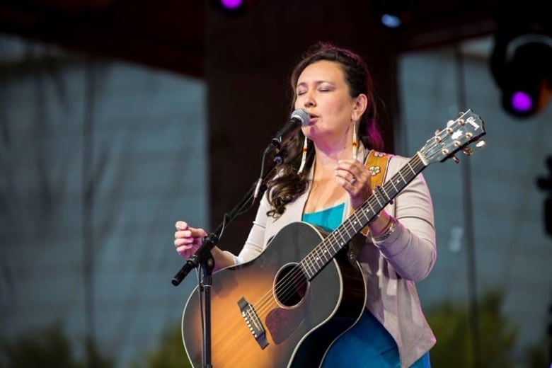 A woman singing into a mic with a guitar.