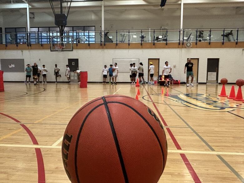 A basketball in focus, with players in a gym in the background. 