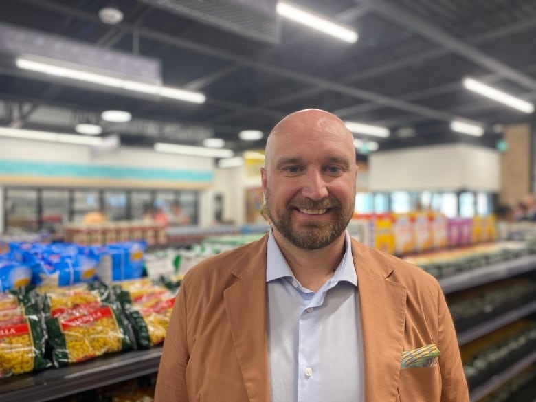 a man wearing a jacket stand in front of a aisle of groceries.