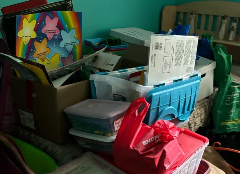 Containers filled with books and school supplies are piled onto a bed in a room. 