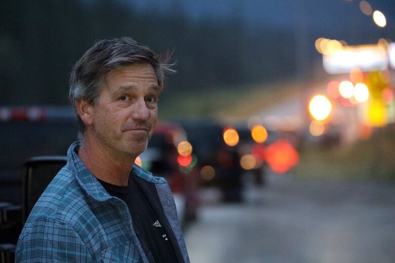 A man in a blue shirt stands on the side of the highway.