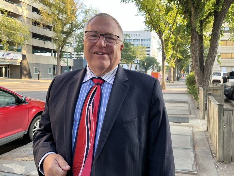 A man in a suit stands on the sidewalk during the day.