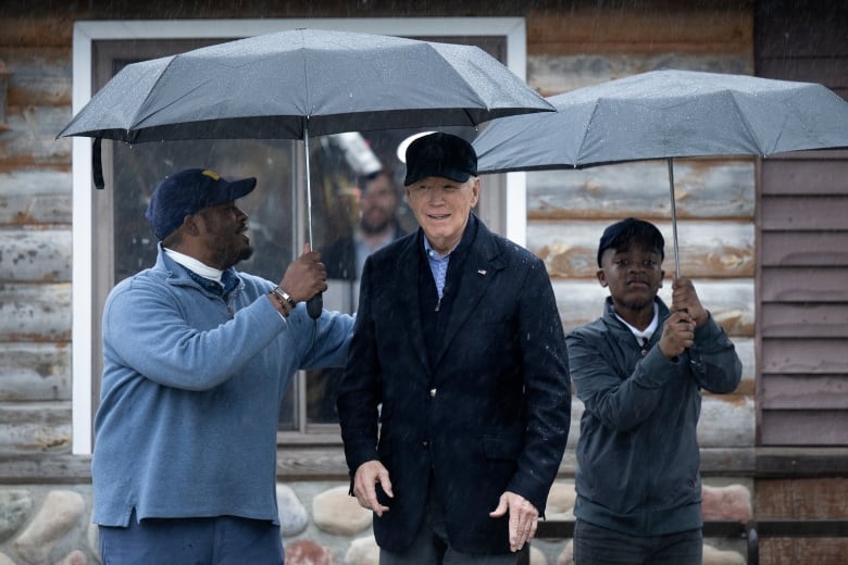 Two people hold umbrellas for a man.