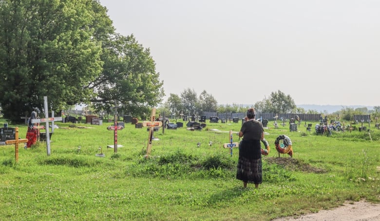 A woman looks towards graves in a cemetery.