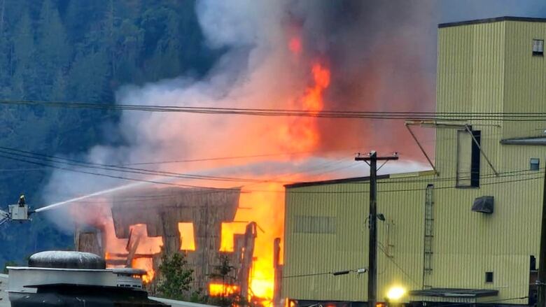 A large fire is seen at a wooden building, with firefighters visible putting it out.