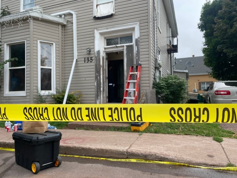 Yellow police tape in the foreground with a beige coloured house in the background.