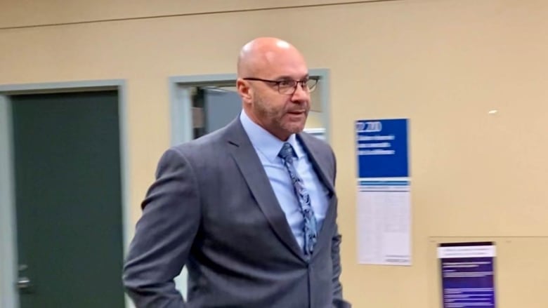 A bald man in a suit and wearing glasses. 