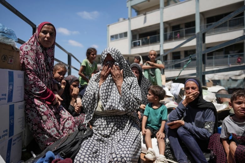 People weep as they sit in the back of a truck.