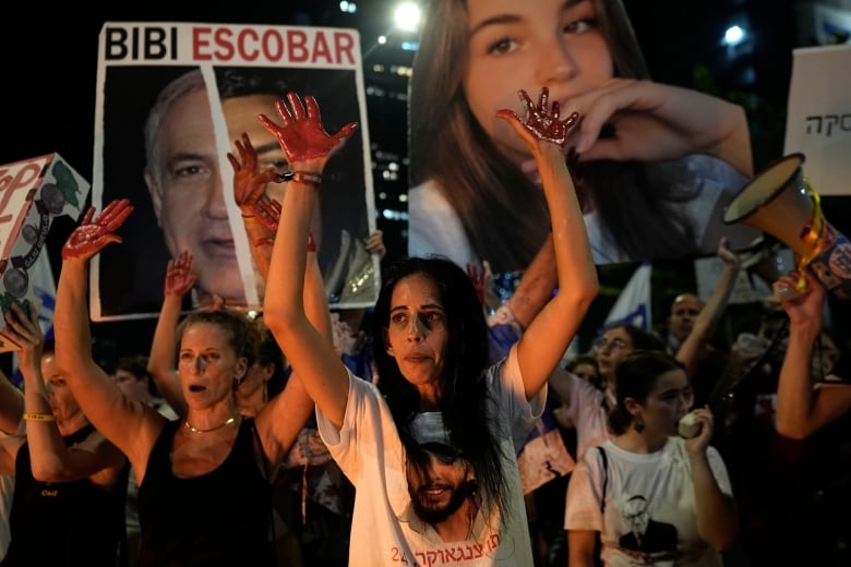 Protesters hold up their hands which they've painted red as others hold up signs of missing people.