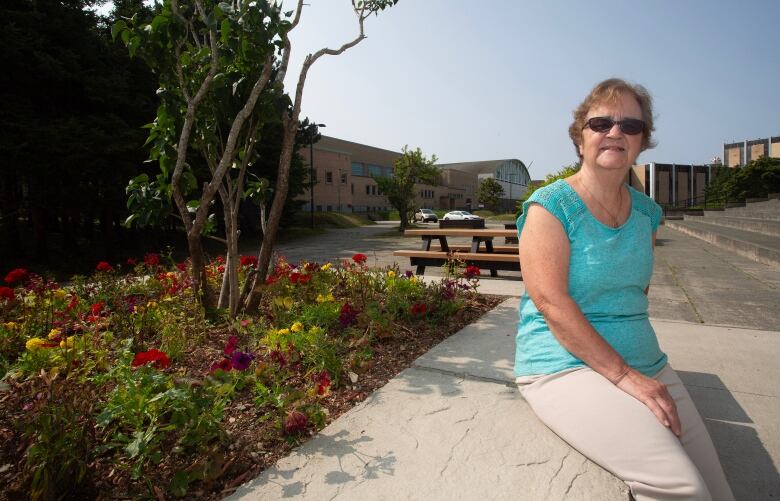 A smiling woman wearing a teal shirt sits on the edge of a flower bed.