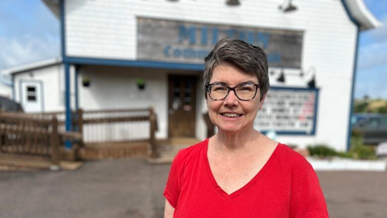 Woman in red shirt standing outside community hall.