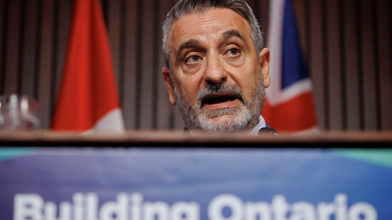 Photo of a man with grey hair speaking at a podium that reads 