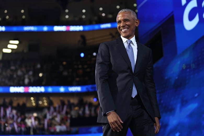 A smiling man with short, grey hair walks across a stage.