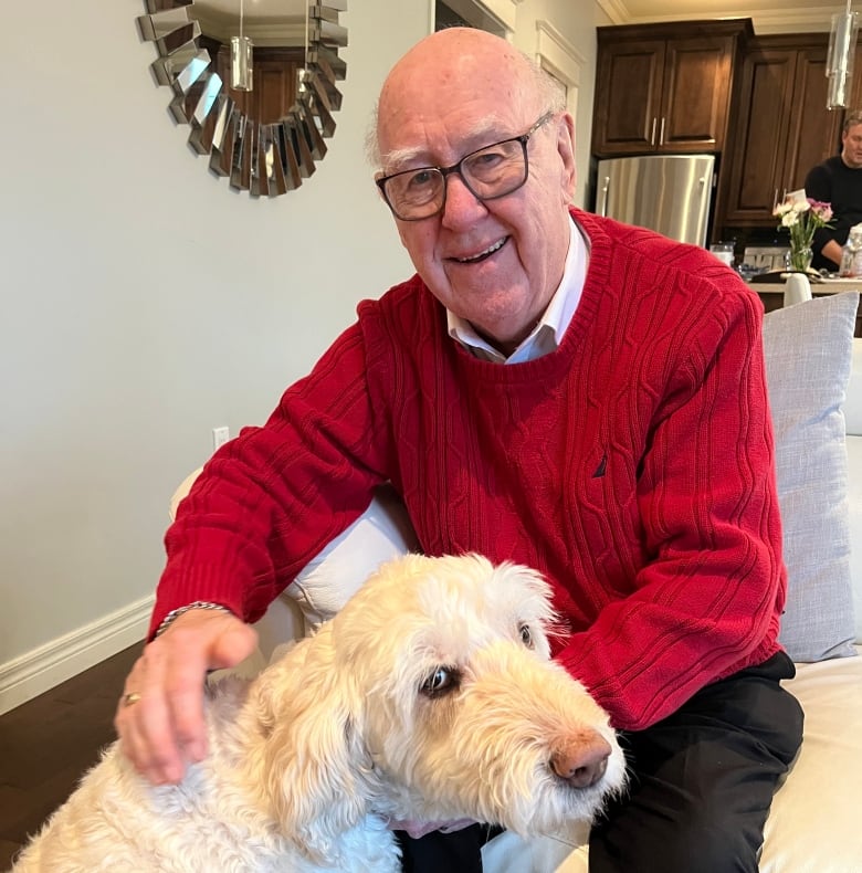 An older man in a red sweater rubs the fur of a dog. 