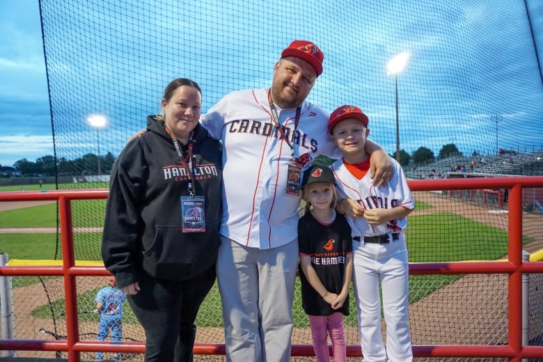 A family poses for a photo with a baseball field in the background