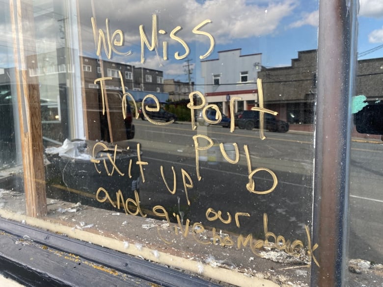 Someone has scribbled in yellow marker on a hotel window: We miss the Port Pub.