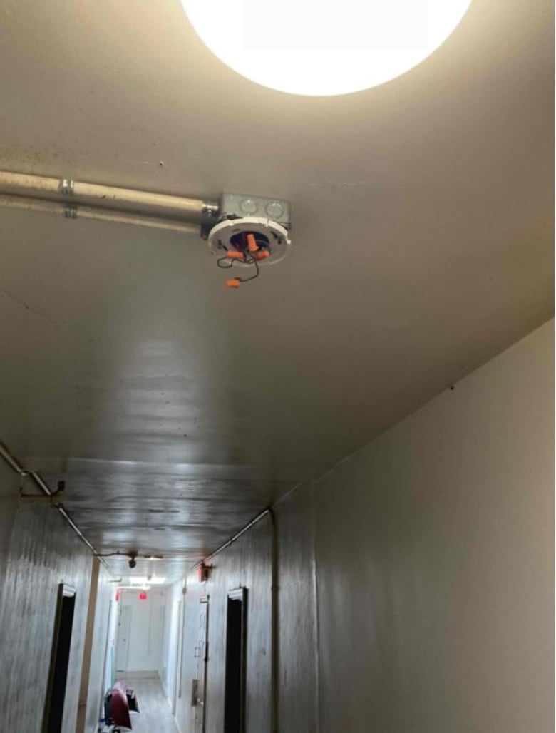 View of a hallway with a shot looking up toward a smoke detector outlet with wires hanging out of it.