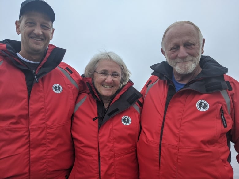 Two men and a lady in the middle, standing shoulder to shoulder wearing red jackets.  