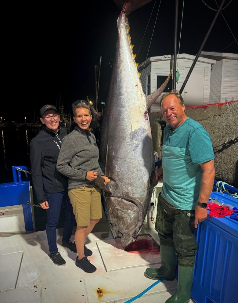 Three people smile standing next to a large bluefin tuna fish. 