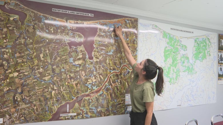 A girl in a green shirt points to the upper right corner of a large map of Prince Edward Island. 