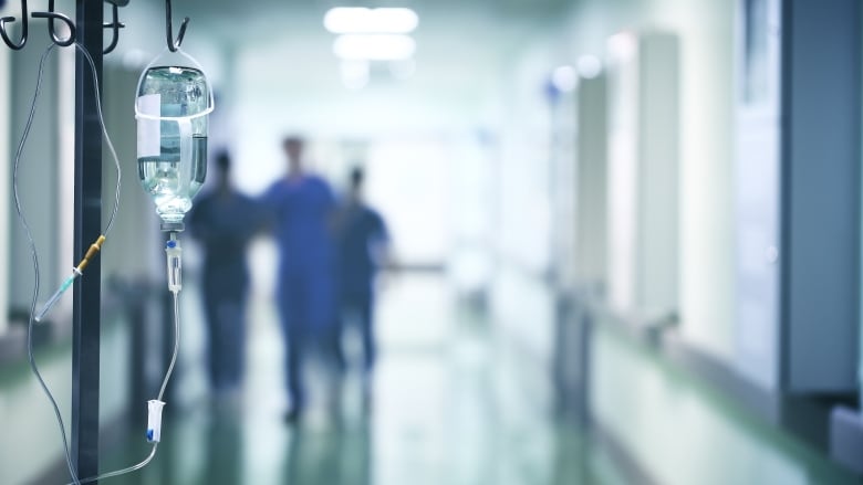 An IV unit is shown in the foreground of a hospital corridor. 