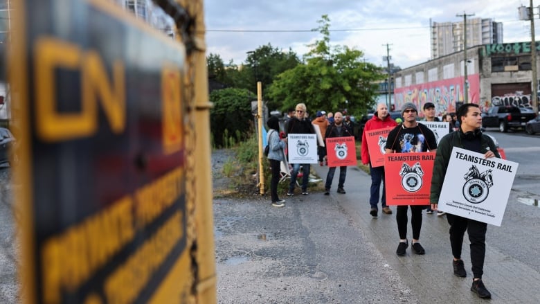 Teamsters union members picketing near a metal fence at the entrance of a lot with a sign that reads: CN provide property; no trespassing.