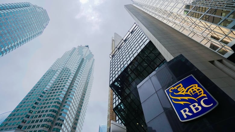 View of the Royal Blank Plaza skyscraper, photographed from below looking up at the sky. The tower gleams gold. A sign featuring he RBC logo is in the foreground.