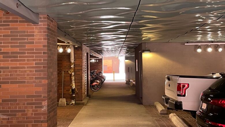 View of a pedestrian passage (ground level) in a parking garage. The ceiling is covered with shiny pale blue fibreglass resembling rippling water.