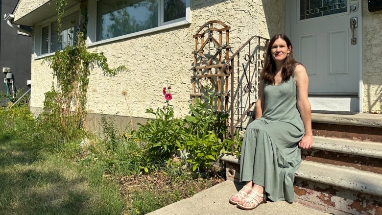 A woman sits on the front step of a bungalow.