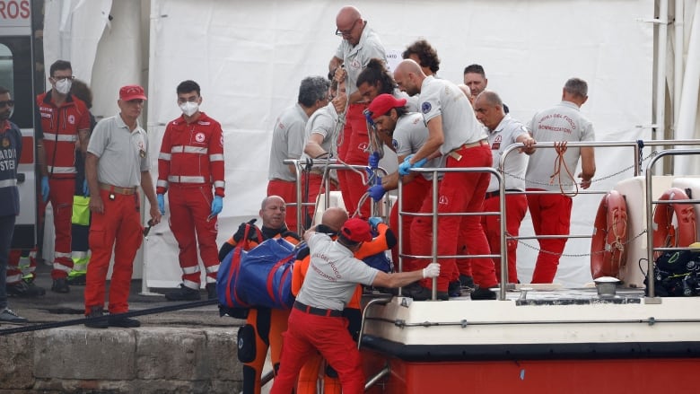 Rescue personnel move a blue body bag onto a red ship.