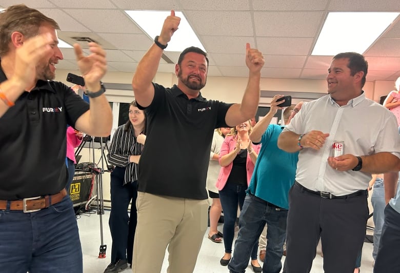 Three man cheer. They are standing in a crowded room.