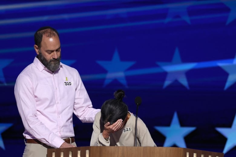 Woman with face buried in lectern, next to husband, on blue convention stage.