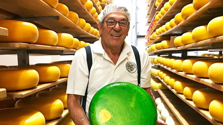 A man stands in between aisles of cheese holding a wheel of gouda.