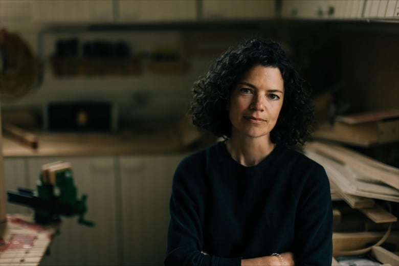 A woman softly smiling. There are wood boards behind her. 