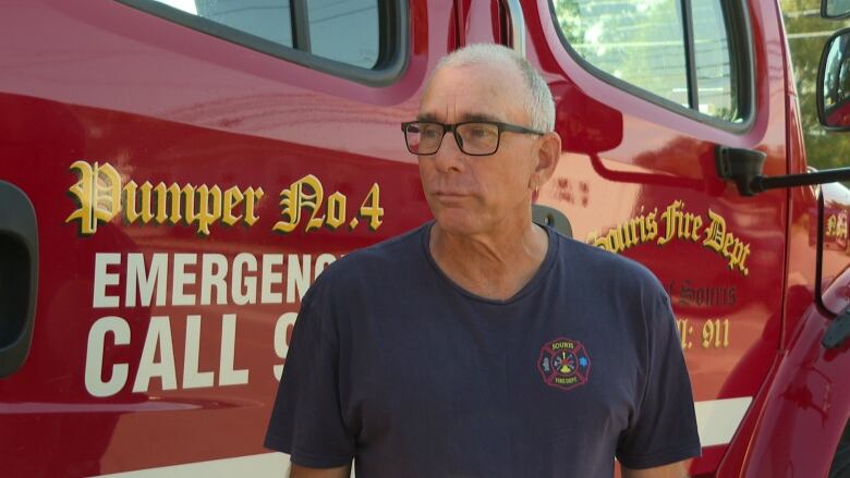 A man in a blue t-shir stands in front of a red fire truck