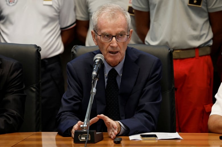 A man sits at a table and speaks into a microphone.