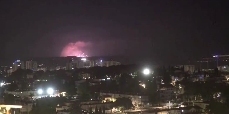 A blast illuminates the dark sky behind a hill and a residential area.