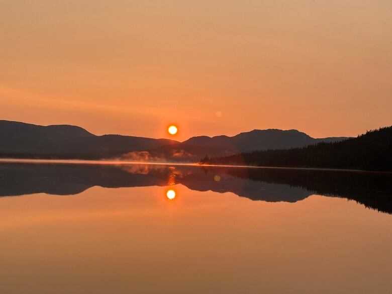 The sun is low over the hills, and reflected in the still surface of the water.