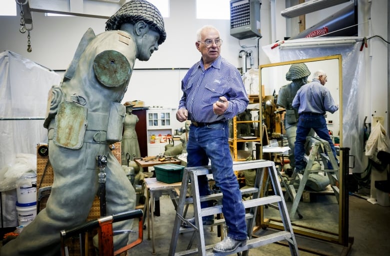 A man stands on a ladder, preparing to work on a large statue.