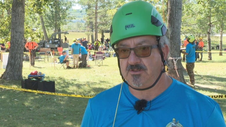 A man with greying facial hair wearing a green helmet, polarized glasses and a blue shirt.