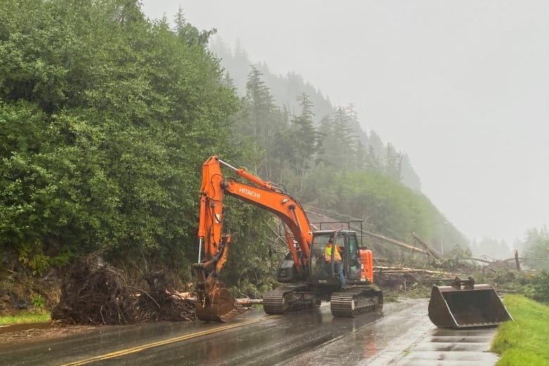 A big orange machine clears debris of fallen trees off a road.