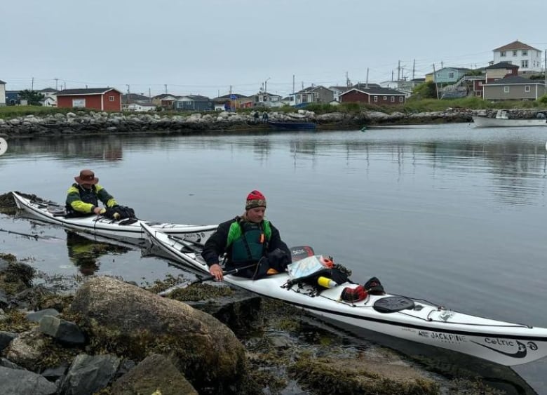 Two men in their kayaks on a bay ringed by colourful houses.