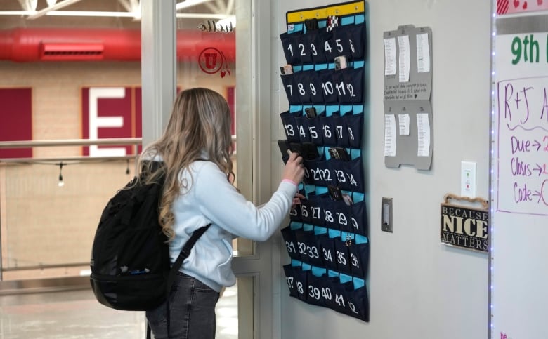 A student places a cellphone in a  storage  unit in a  classroom