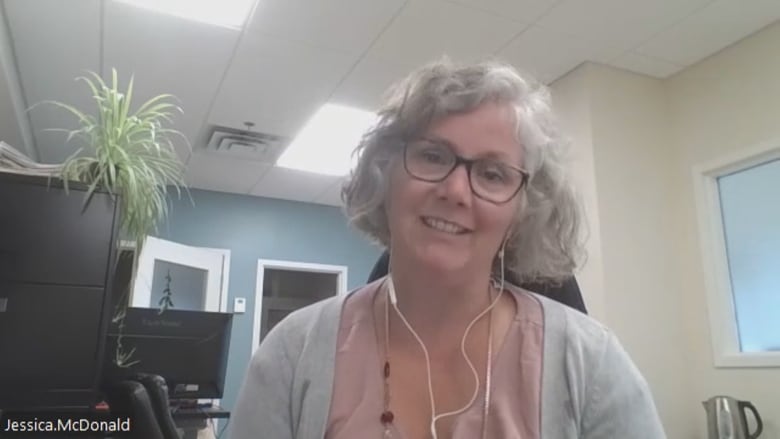 A Caucasian woman with glasses and short curly hair.