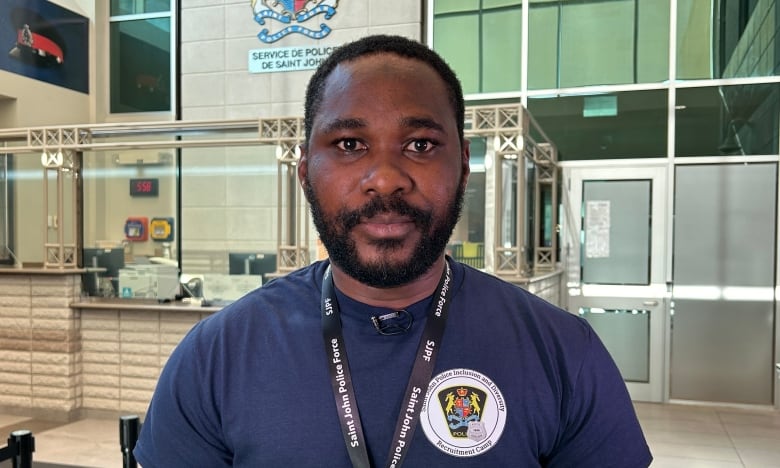 A black man with black hair and beard, wearing a blue t-shirt.