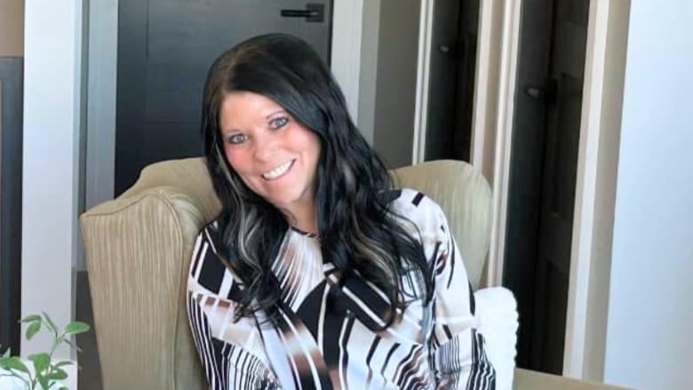 Woman with black hair sits in chair, looking at the camera and smiling